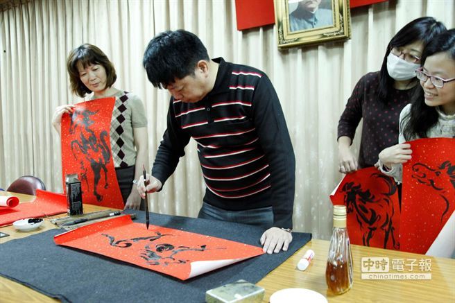 中山大學劇場藝術學系副教授王以亮（中）以酒墨揮毫畫春聯。（曹明正攝）(另開新視窗/jpg檔)圖片